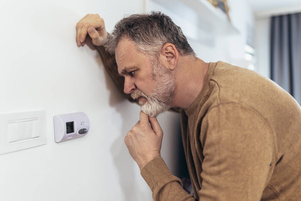 Uomo maturo che regola la temperatura del riscaldamento centrale a casa sul termostato - Foto, immagini