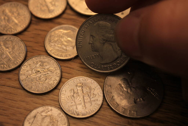 рука збирає чверть монети в американській валюті, розкладеній на дерев'яній підлозі
 - Фото, зображення