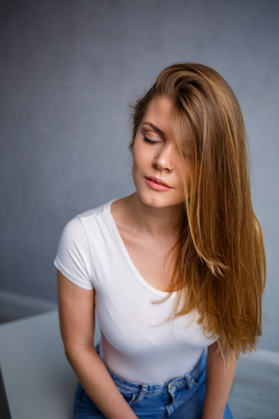 Ritratto di una giovane bella donna dai capelli biondi di aspetto europeo. Vestita con una maglietta bianca. Foto emotiva di una persona - Foto, immagini
