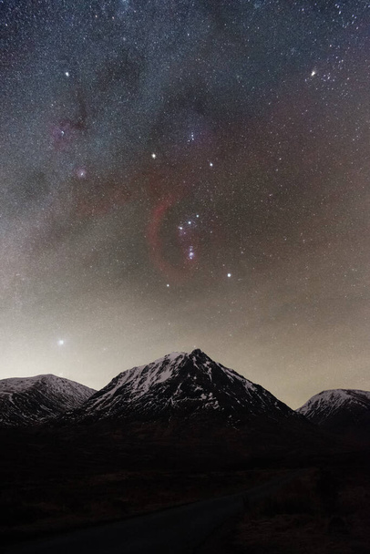 Glen Etive astrofotografía con la Vía Láctea y Orión elevándose por encima de una montaña nevada - Foto, Imagen