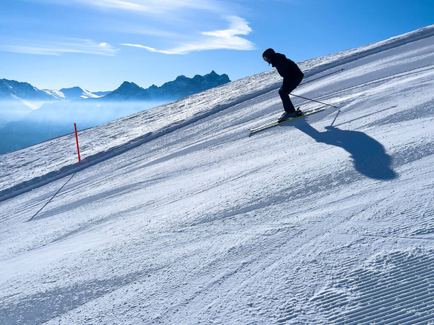 a skier with black ski gear is skiing down the slope under blue sky - Fotoğraf, Görsel