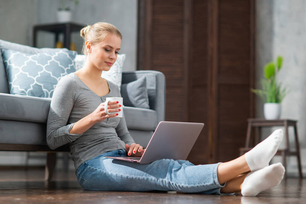 Young woman works using a laptop while sitting on the floor at home. Student, entrepreneur or freelancer girl working or studying remotely via internet. - Photo, image