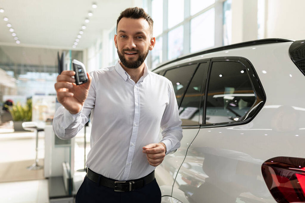 продавец автомобиля передает ключи от нового внедорожника покупателю в автосалоне - Фото, изображение