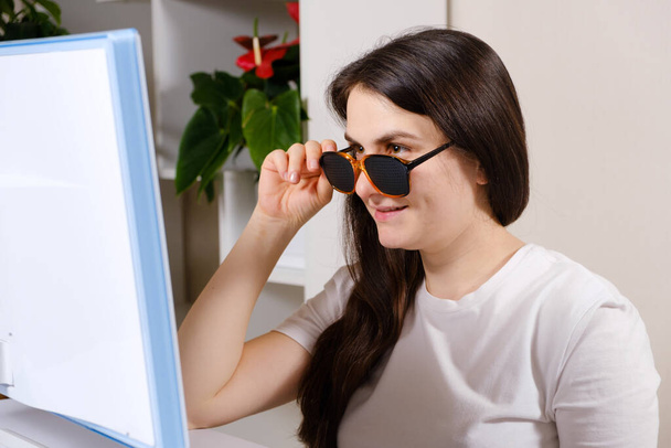 Una mujer mira una pantalla de ordenador a través de vidrios perforados con agujeros para mejorar la visión en astigmatismo y queratocono - Foto, Imagen