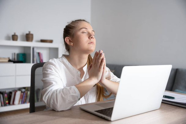 Young woman praying in front of laptop - Фото, зображення
