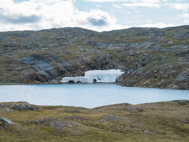 Northern landscape, tundra in Swedish Lapland with blue artic lake with reamains of melting snow cave, green hills and mountains at Padjelantaleden hiking trail. Summer day, blue sky, white clouds - Photo, Image