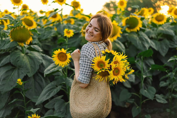 Piękna młoda kobieta ze słonecznikami ciesząca się naturą i śmiejąca się na letnim polu słonecznika. - Zdjęcie, obraz