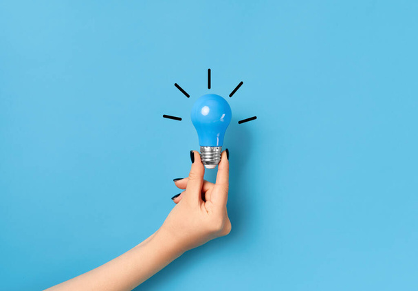 Female hand hold light bulb on blue background with copy space for text - Photo, image