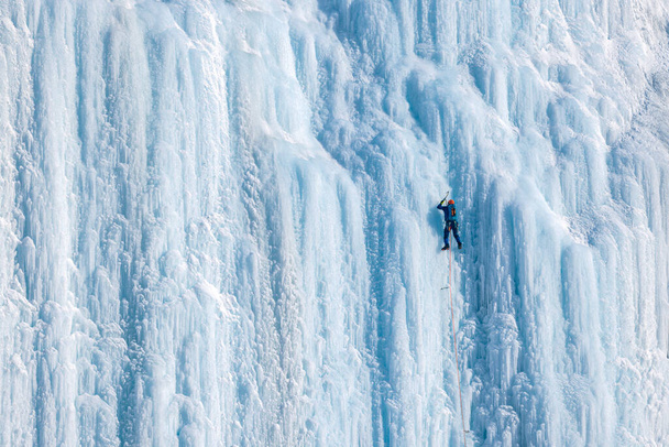 Ο αναρριχητής πάγου σκαρφαλώνει τον κάθετο τοίχο. Οι αθλητές απολαμβάνουν την ύπαιθρο σκαρφαλώνοντας στον τοίχο του πάγου. Ενεργοί άνθρωποι που απολαμβάνουν αδρεναλίνη σπορ. - Φωτογραφία, εικόνα