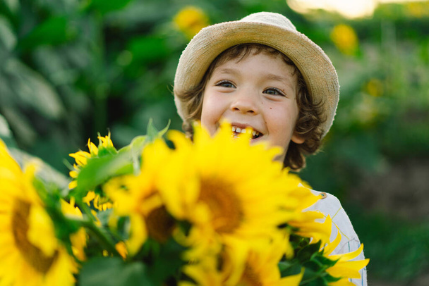 Boldog fiú sétál a napraforgóban. Gyermek játszik nagy virág és szórakozás. - Fotó, kép