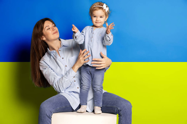 Portrait of young woman, mother with her little girl, daughter isolated over blue and yellow Ukrainian flag background. Free Ukraine - Foto, Imagen
