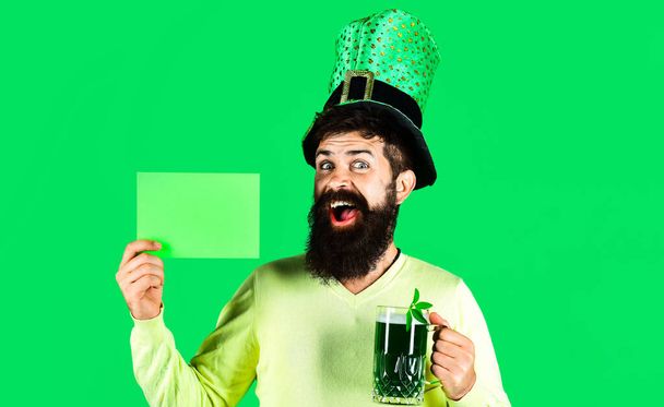 Patricks Day. Glücklicher bärtiger Mann mit Hut und grünem Bier hält Tafel mit Kopierfläche für Werbung. - Foto, Bild