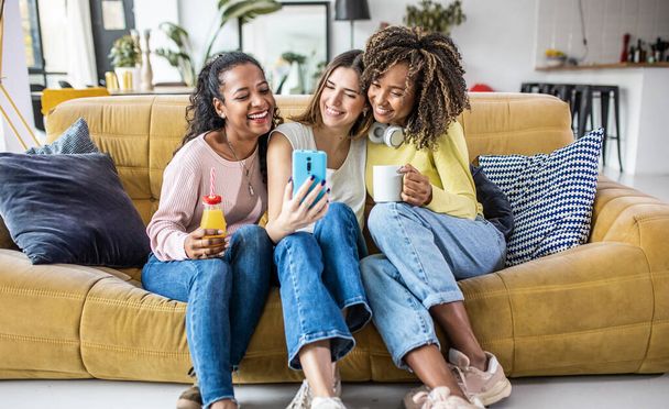 Trzy młode, wielorasowe kobiety robią sobie selfie relaksując się razem w domu - Zdjęcie, obraz