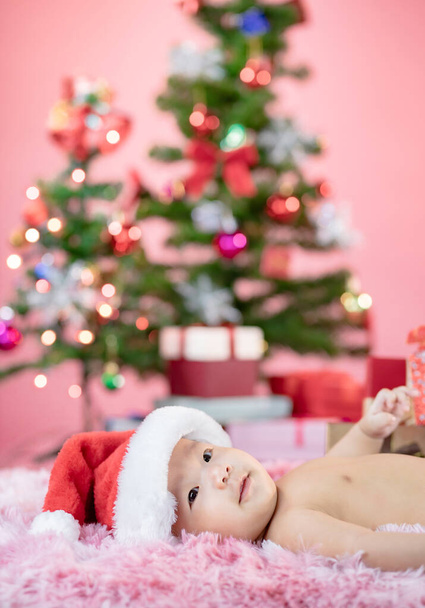 Ευτυχισμένο χαριτωμένο μωρό φορώντας καπέλο Σάντα με ροζ φόντο τα Χριστούγεννα - Φωτογραφία, εικόνα
