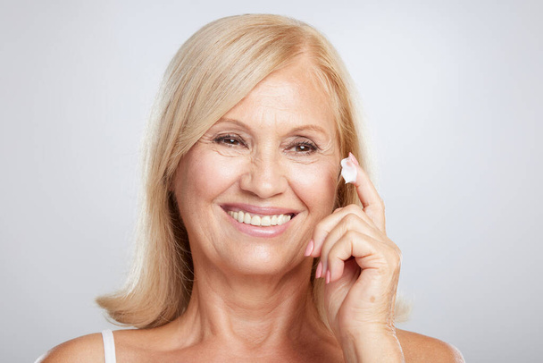 An attractive blond senior woman putting anti-age creme. Beauty photography - Фото, изображение