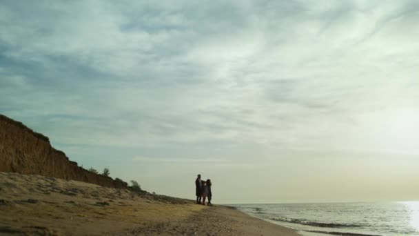 İnsanlar ayakta duran plaj manzarası grubu. Aile gün batımında yürür dalgalar çarpar. - Video, Çekim