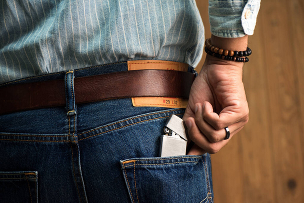 The man put the brushed chrome lighter with windproof into his jeans. - 写真・画像