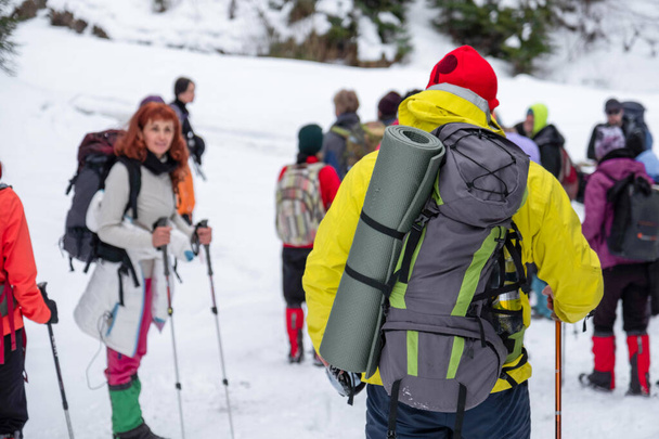 Felvételek egy tapasztalt középkorú férfi túrázó hátáról sárga sí jelmezben és fényes színes kalapban. Téli szezonban, a túra borított hó és más túrázók a háttérben - Fotó, kép