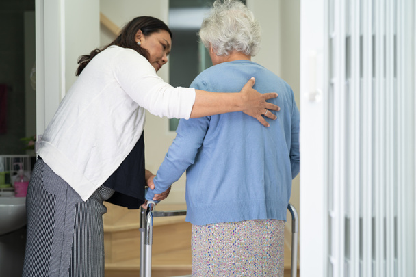 Pflegehelferin hilft alter Frau mit Rollator die Treppe im Haus hinauf. - Foto, Bild