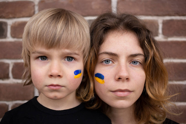 volti di ragazzo e giovane donna con bandiera blu e gialla dipinta sulle guance. Famiglia, unità, sostegno. Gli ucraini sono contro la guerra. chiedere aiuto alla comunità mondiale. Stand con ucraina - Foto, immagini