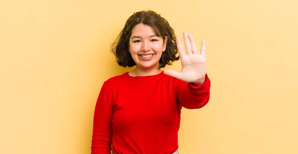 pretty hispanic woman smiling and looking friendly, showing number five or fifth with hand forward, counting down - Foto, imagen