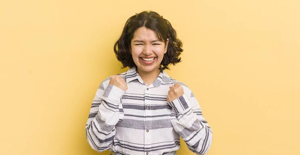 mujer bastante hispana gritando triunfalmente, riendo y sintiéndose feliz y emocionada mientras celebra el éxito - Foto, imagen