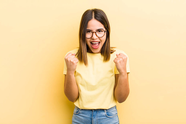 pretty hispanic woman shouting triumphantly, laughing and feeling happy and excited while celebrating success - Foto, afbeelding