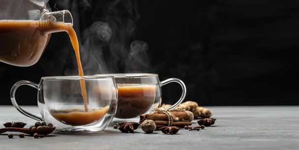 Indiai masala chai tea. Forró masala chai fűszeres tea tej és fűszerek öntjük egy pohár sötét alapon. Hosszú banner formátum. a szöveg helye. - Fotó, kép
