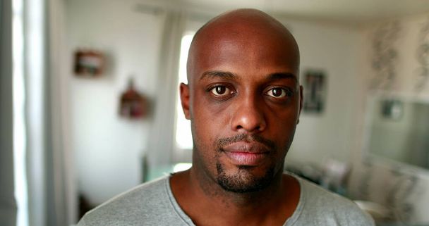 Black African man portrait looking at camera in living-room home, serious expression - 写真・画像