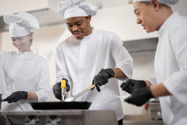 Equipo multirracial de cocineros profesionales en uniforme preparando comidas para un restaurante en la cocina - Foto, Imagen