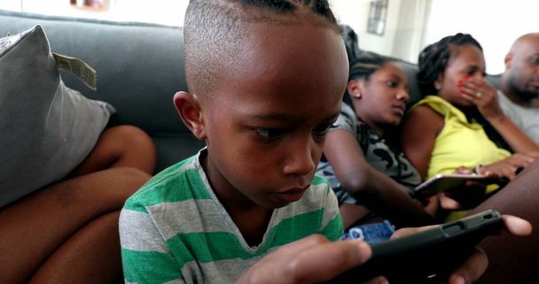 Afrikkalainen perhe käyttää teknologialaitteita kotona, mustat vanhemmat ja lapset etsivät älypuhelimia ja kannettavaa tietokonetta - Valokuva, kuva