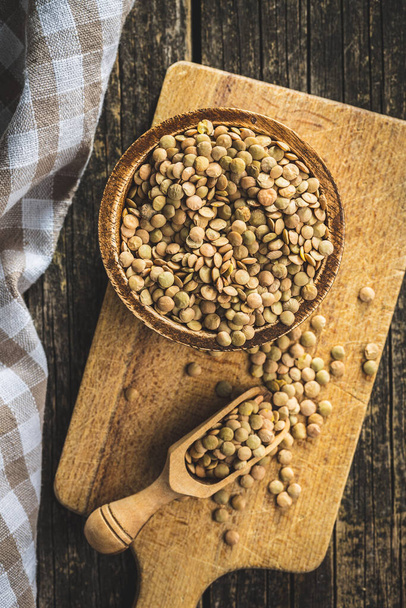 Uncooked brown lentils. Raw legume in a bowl on cutting board. Top view. - Fotografie, Obrázek