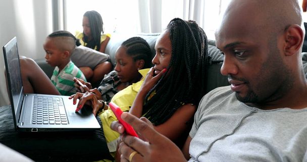 Afrikaanse familie op zoek naar laptop en mobiele telefoon apparaten thuis bank - Foto, afbeelding