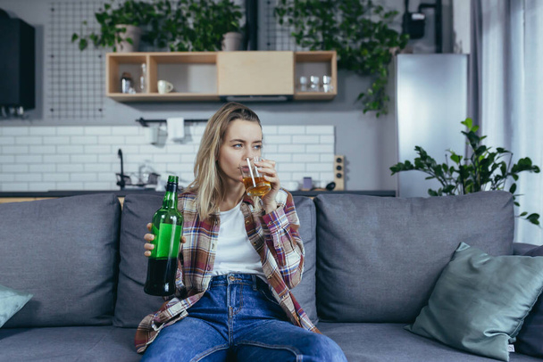 Woman alone at home, grief and depression, drinking strong alcohol, alcoholic sitting at home on the couch - Фото, изображение
