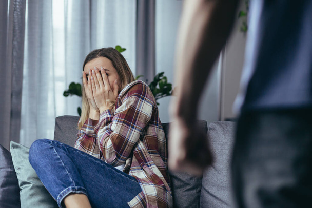 Domestic violence, angry husband shouting and beating woman, close-up photo, wife crying sitting on sofa - Φωτογραφία, εικόνα