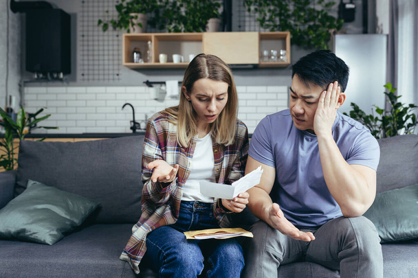 Multiracial couple, Asian man and woman, together at home, received a letter with bad news, frustrated and sad sitting on the couch at home - Foto, Imagem