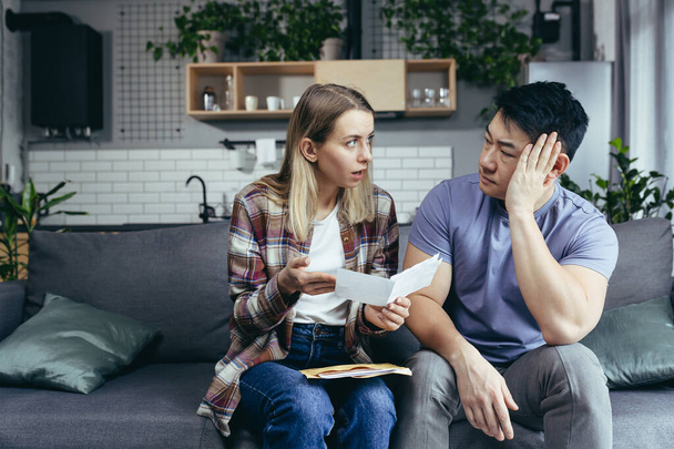 Multiracial couple, Asian man and woman, together at home, received a letter with bad news, frustrated and sad sitting on the couch at home - Foto, immagini