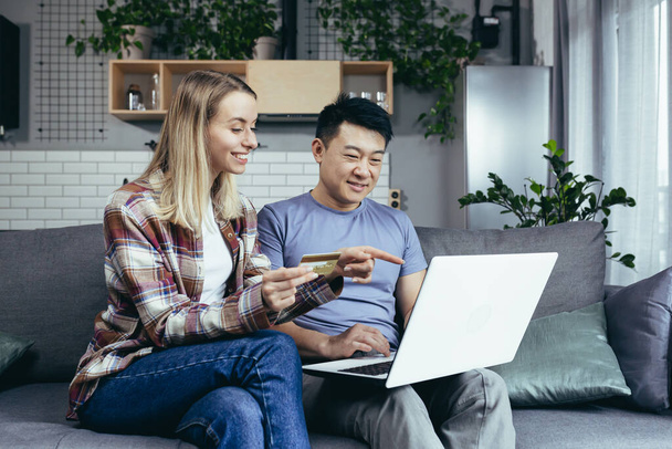Young happy asian couple and woman, together at home, shopping online, using laptop and bank credit card, happy family - Foto, afbeelding