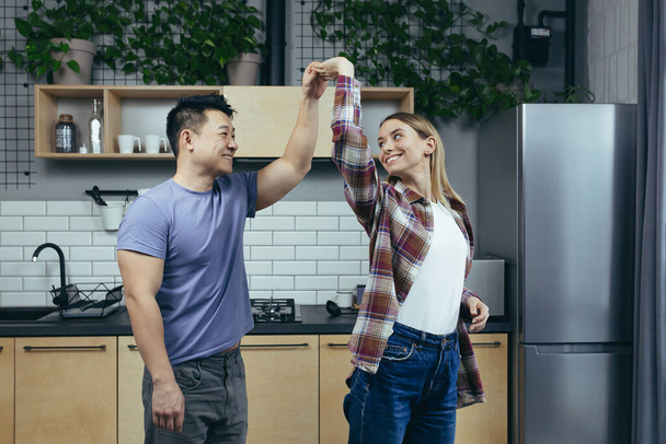 Homem e mulher dançando juntos, se divertindo em casa, na cozinha, uma família multirracial - Foto, Imagem