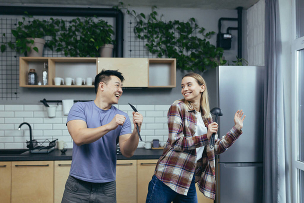 Man and woman dancing together, having fun at home, in the kitchen, a multiracial family - Foto, Imagen