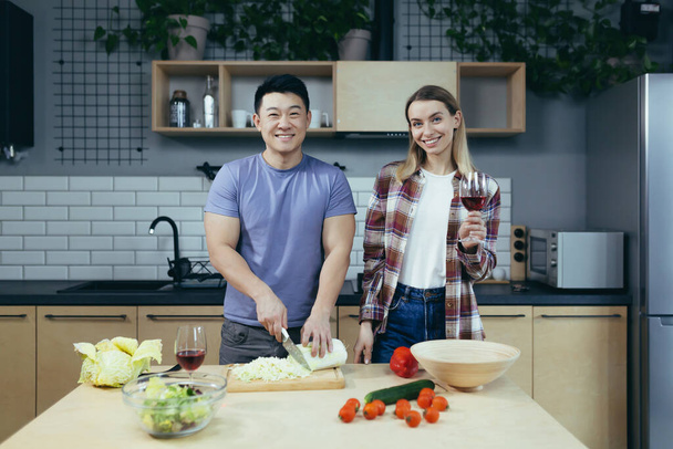 Happy young family, man and woman, cooking together, Asian cuts vegetables, date at home, romantic evening - Foto, imagen