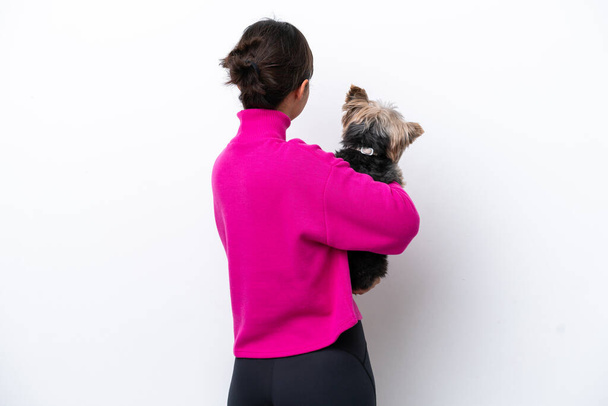 Joven mujer hispana sosteniendo a un perro aislado sobre fondo blanco en posición trasera - Foto, imagen