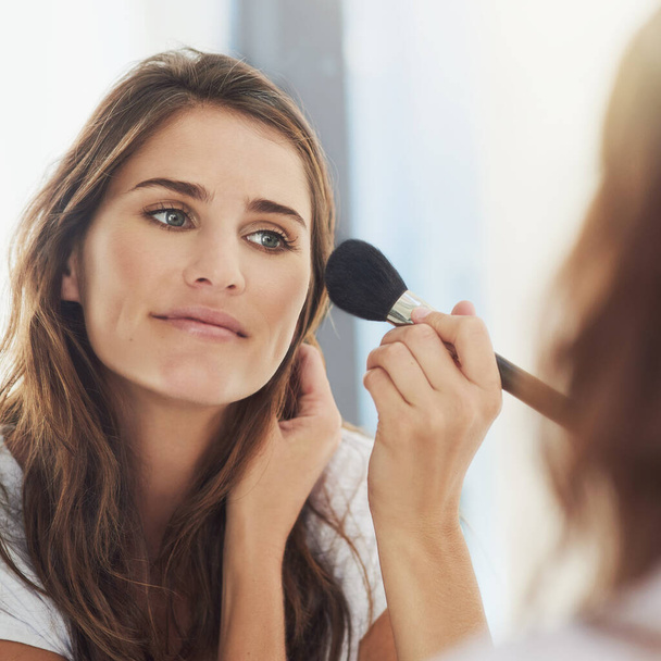 Blending her makeup for a natural look. Shot of a beautiful young woman applying makeup with a brush. - Foto, afbeelding