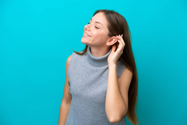 Молода литовська жінка ізольована на синьому фоні, слухаючи щось, поклавши руку на вухо. - Фото, зображення