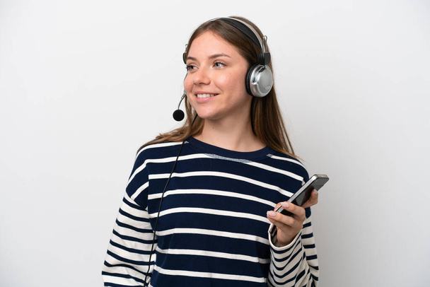 Telemarketer caucasian woman working with a headset isolated on white background keeping a conversation with the mobile phone with someone - Photo, image