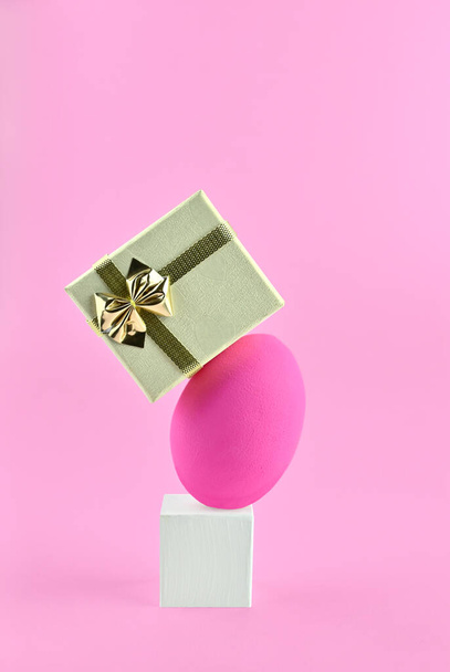 Levitazione da un uovo, un podio e una scatola regalo. Equilibrio uova su uno sfondo rosa. - Foto, immagini