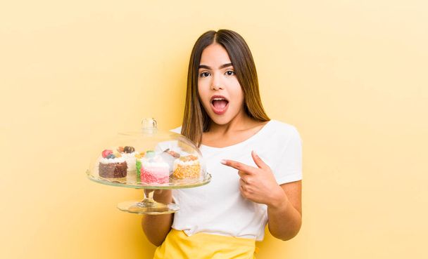 pretty hispanic girl looking excited and surprised pointing to the side. home made cakes concept - Foto, Imagem