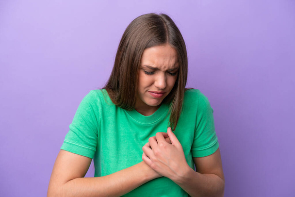 Young caucasian woman isolated on purple background having a pain in the heart - Фото, изображение
