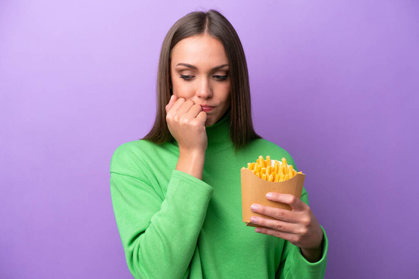Молода біла жінка, що тримає смажені чіпси на фіолетовому фоні, має сумніви
 - Фото, зображення