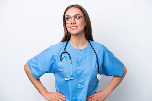 Young nurse caucasian woman isolated on white background posing with arms at hip and smiling - Φωτογραφία, εικόνα